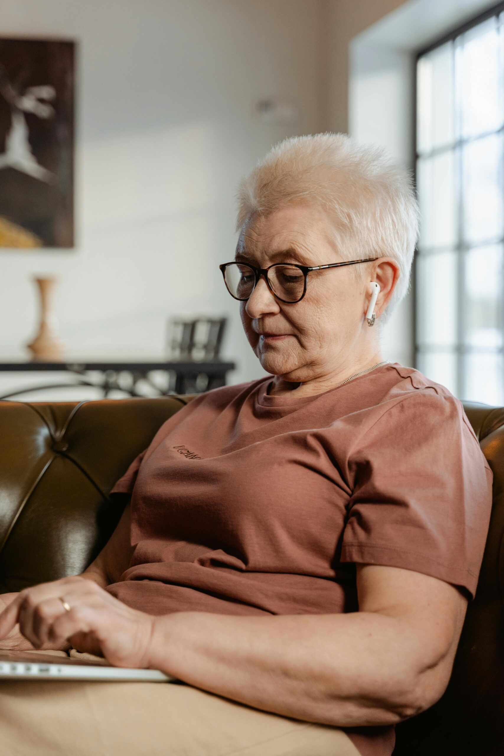 Elderly woman using a laptop indoors, showcasing modern technology use in daily life.